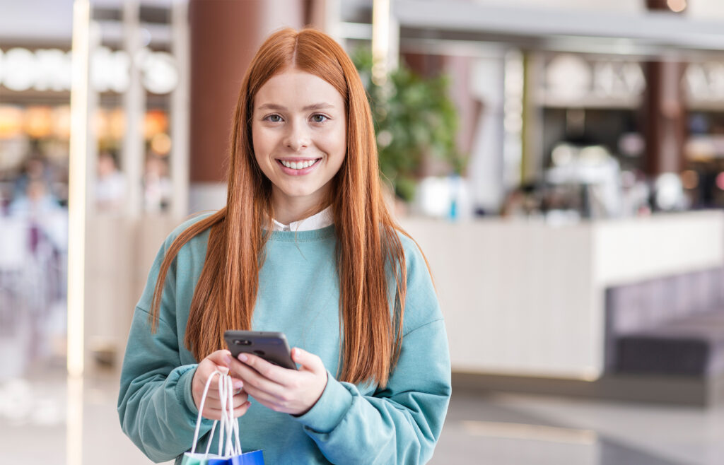 Consumidora sorridente com celular e sacolas de compras exemplifica uma persona de compradora moderna.