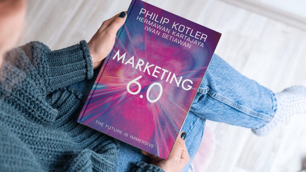 Pessoa segurando o livro Marketing 6.0, de Philip Kotler, Hermawan Kartajaya e Iwan Setiawan, com foco na evolução do marketing digital e imersivo.